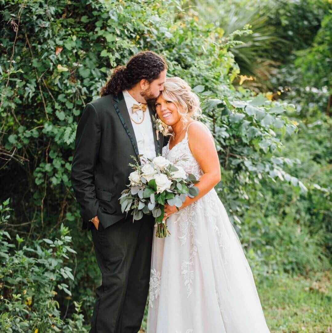 Bride and groom sharing a tender moment outdoors surrounded by greenery.