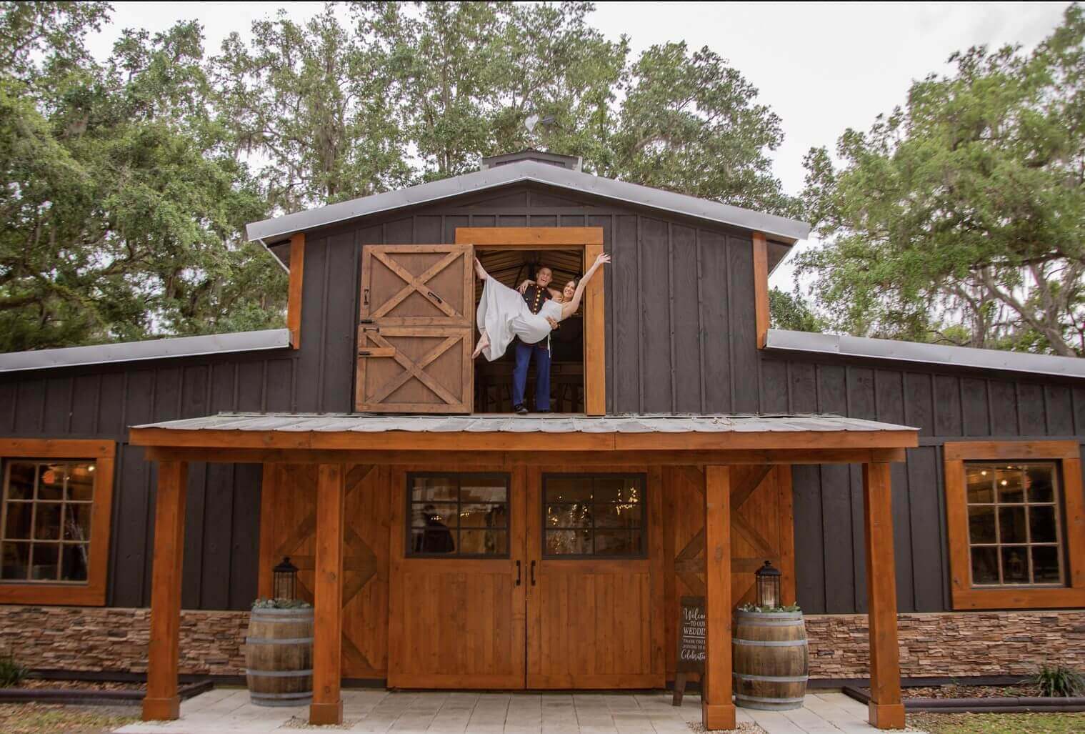 Person leaning out of a barn window with wooden doors below.