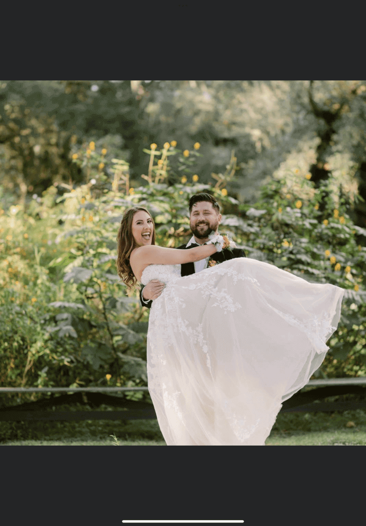 Groom lifts bride joyfully outdoors in a lush garden setting.