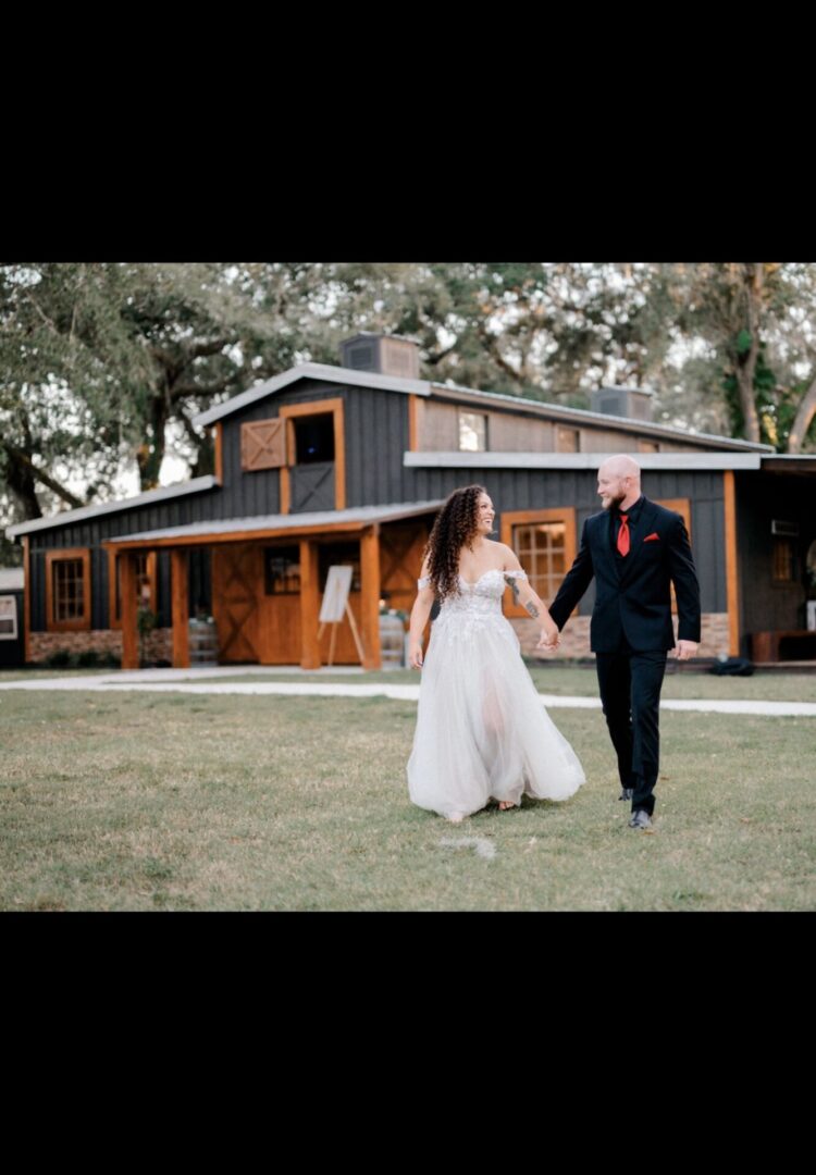 Bride and groom walking hand in hand outside a rustic house.