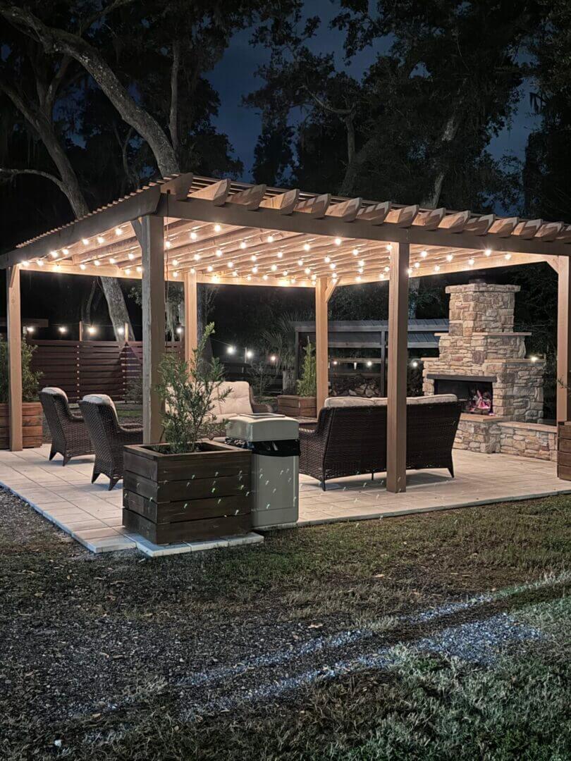 A cozy outdoor pergola with string lights and seating at night.