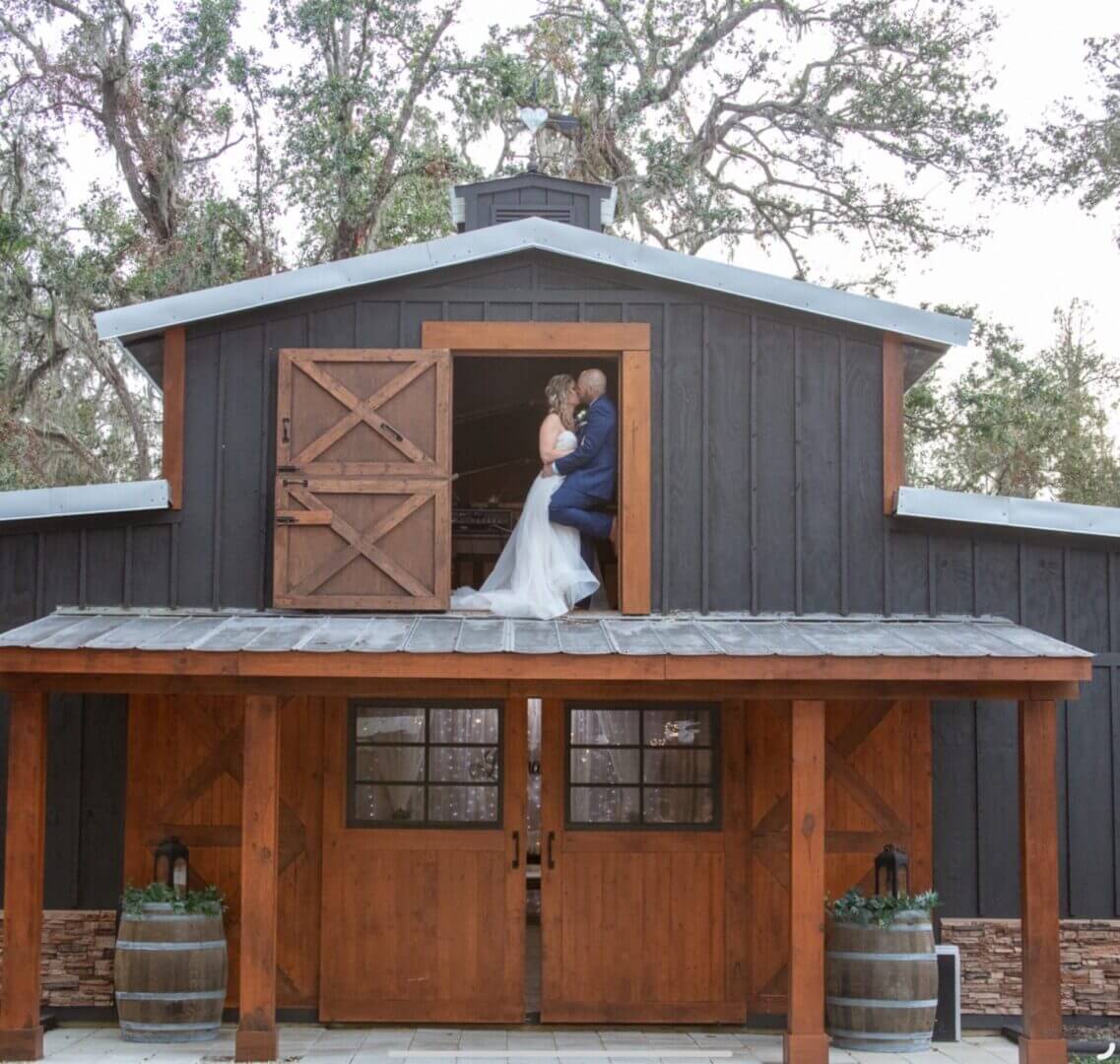Bride and groom embracing on a barn balcony.