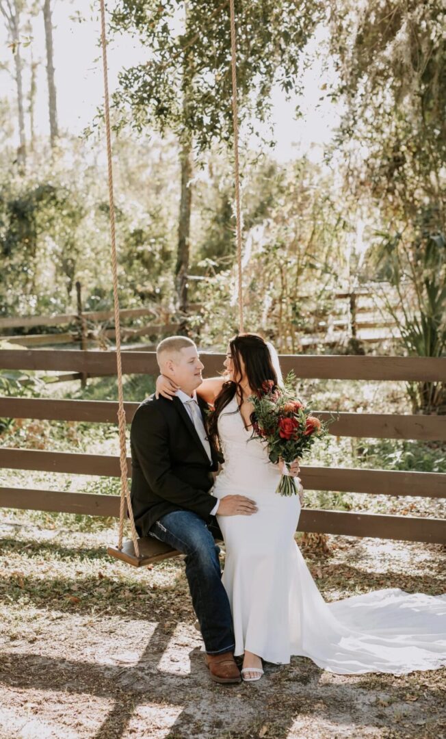 A couple sitting on a wooden fence, sharing a tender moment outdoors.