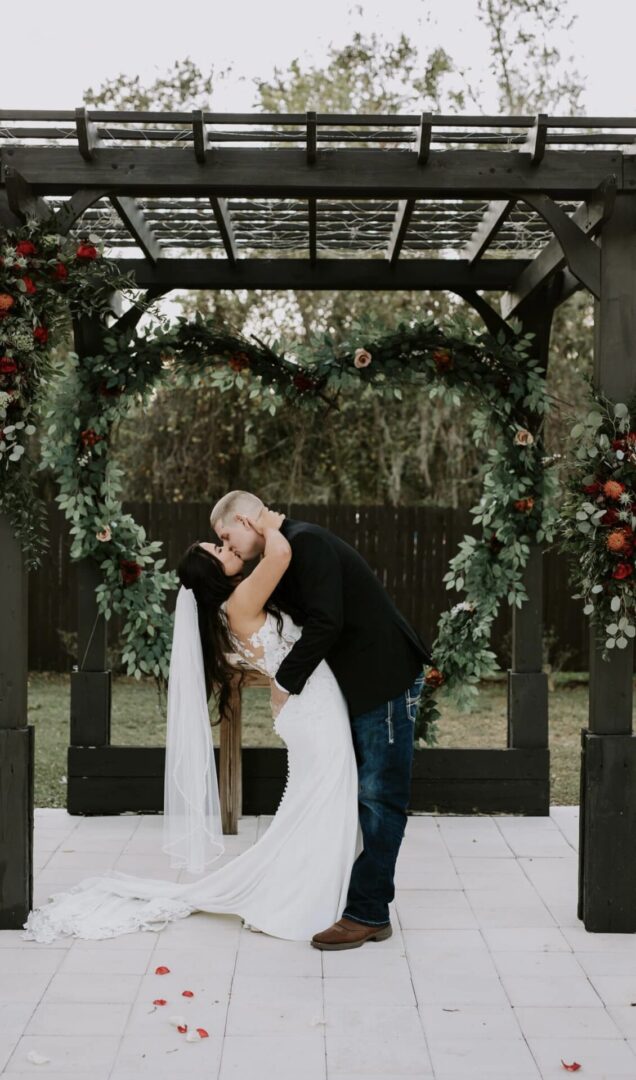 Couple sharing a romantic kiss under a floral arch at their wedding.