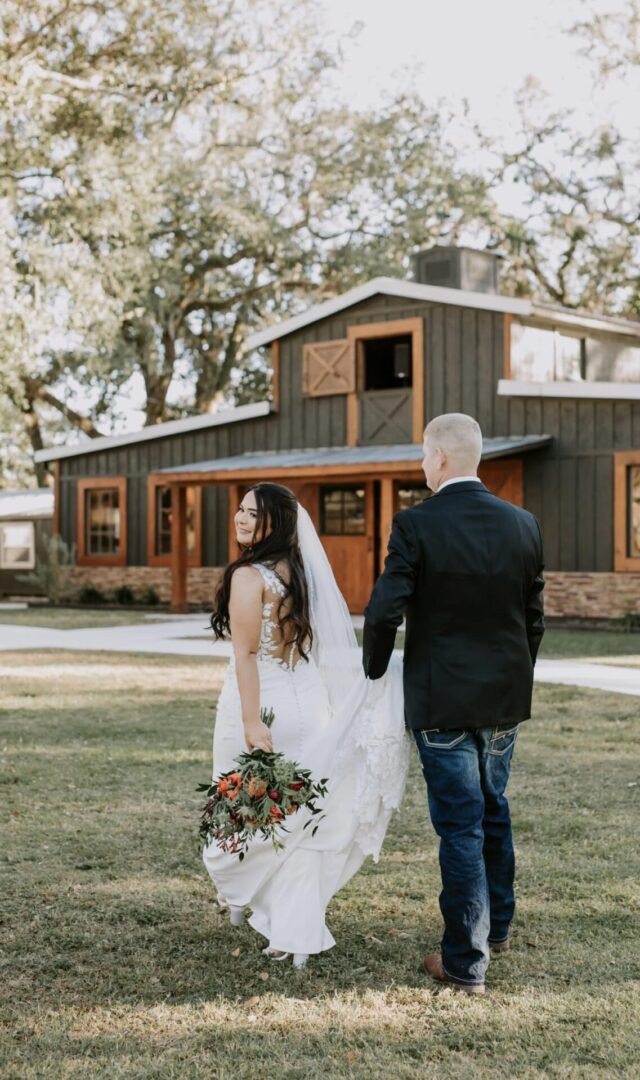 Bride and groom walking hand in hand outside a rustic house.