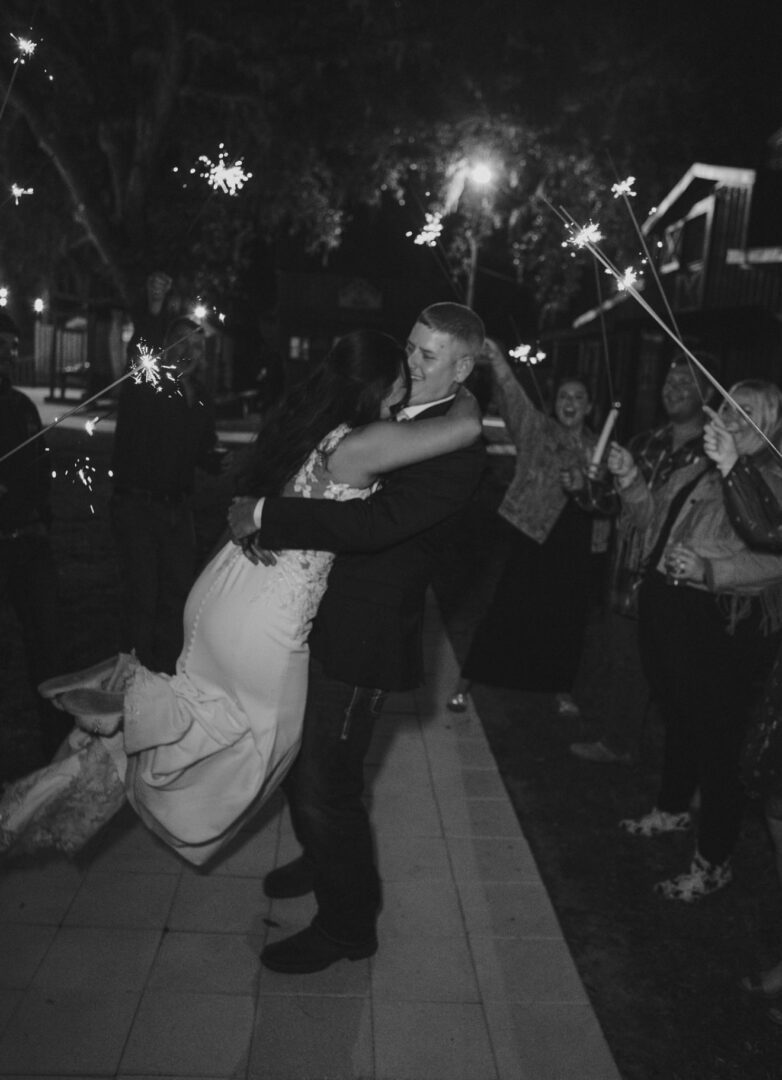 A couple share a joyous embrace at a nighttime celebration with sparklers.