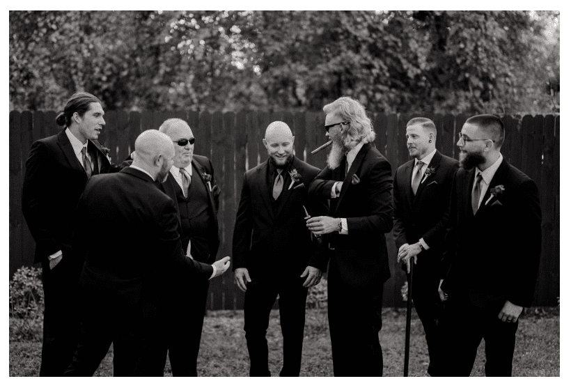 Group of men in formal suits laughing outdoors at an event.