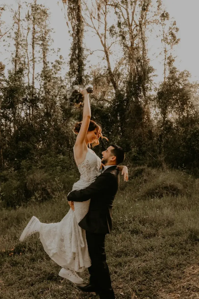 Bride lifted by groom in forest setting.