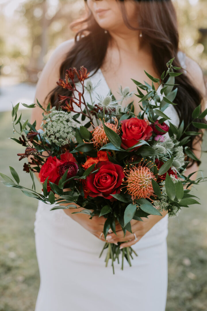 Bride holding a bouquet with red flowers.