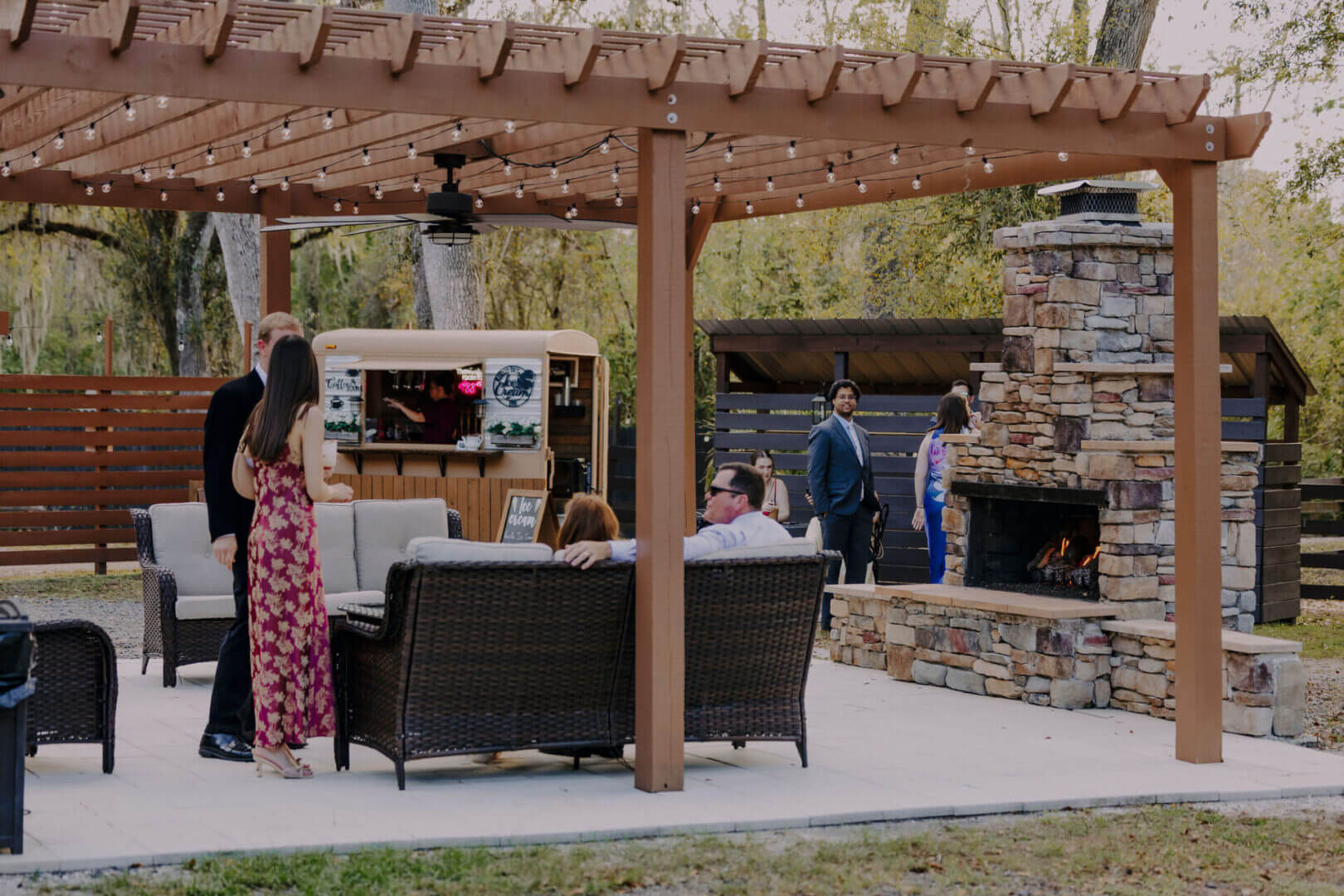 Outdoor gathering under pergola with fireplace.