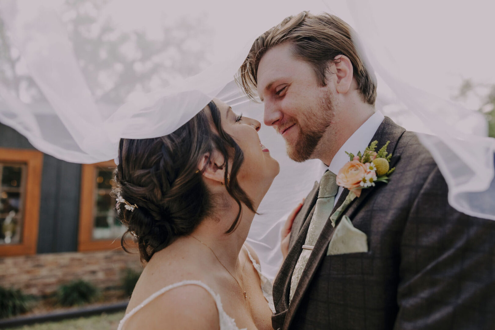 Bride and groom under wedding veil, smiling.