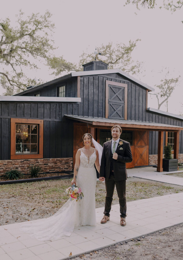 Bride and groom standing in front barn.