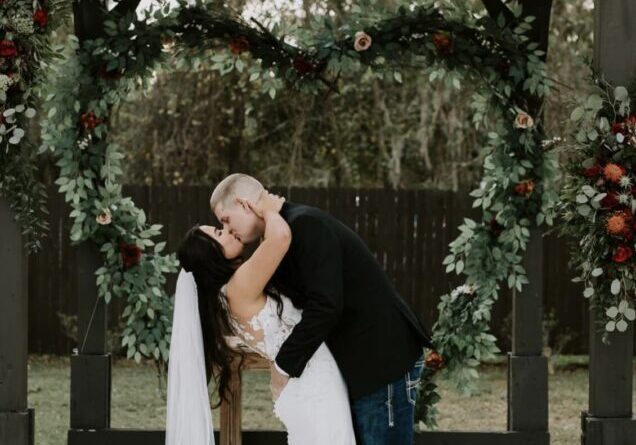 Bride and groom kissing under floral arch.