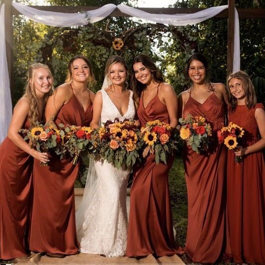 Bride with bridesmaids in rust-colored dresses holding sunflower bouquets.